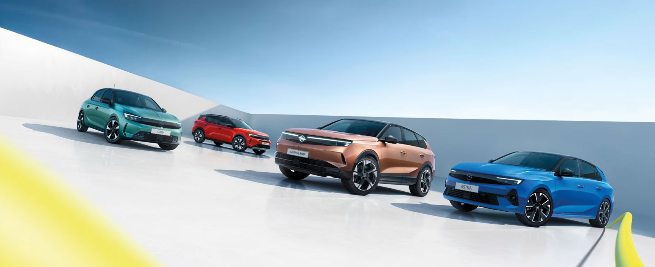 Vier aktuelle Opel Modelle in einer modernen Szenerie: grüner Opel Corsa, roter Opel Frontera, kupferfarbener Opel Grandland und blauer Opel Astra.